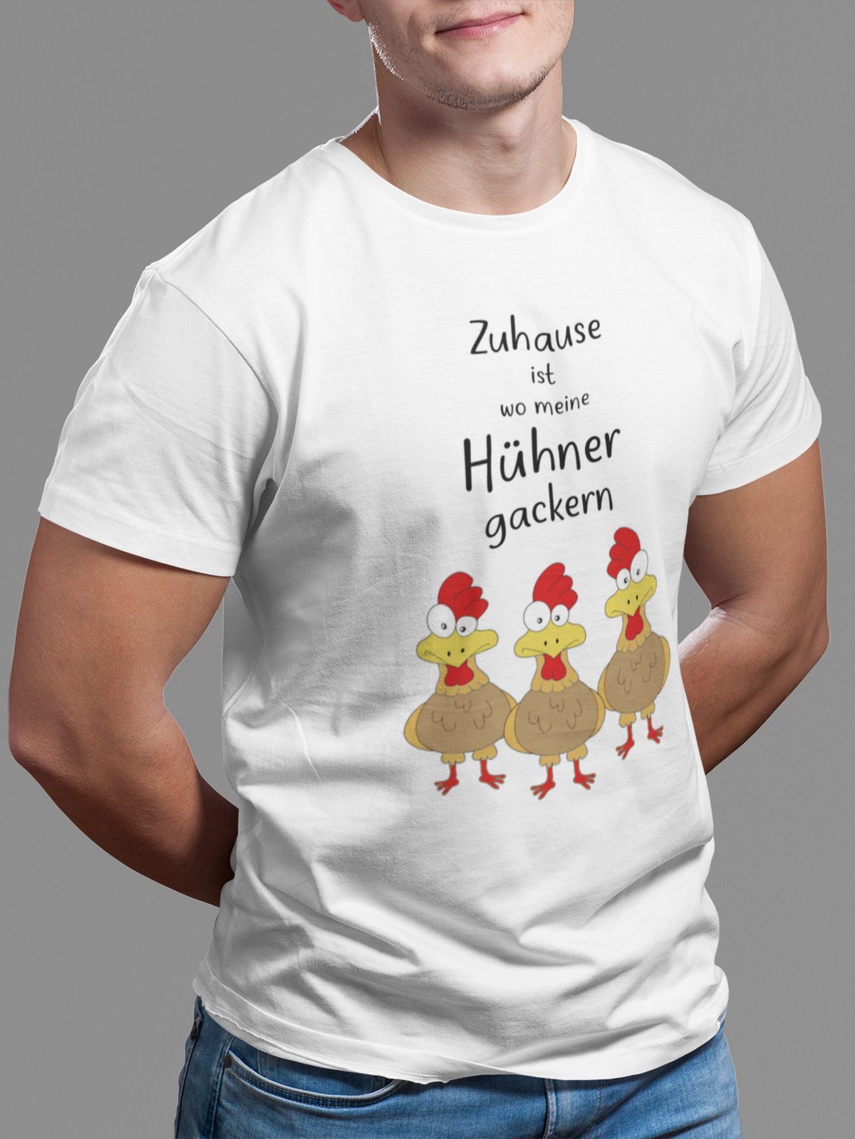 Junger Mann trägt weißes T-Shirt mit buntem Motiv von drei lustigen Hühnern und dem Spruch „Zuhause ist, wo meine Hühner gackern.“ auf der Vorderseite