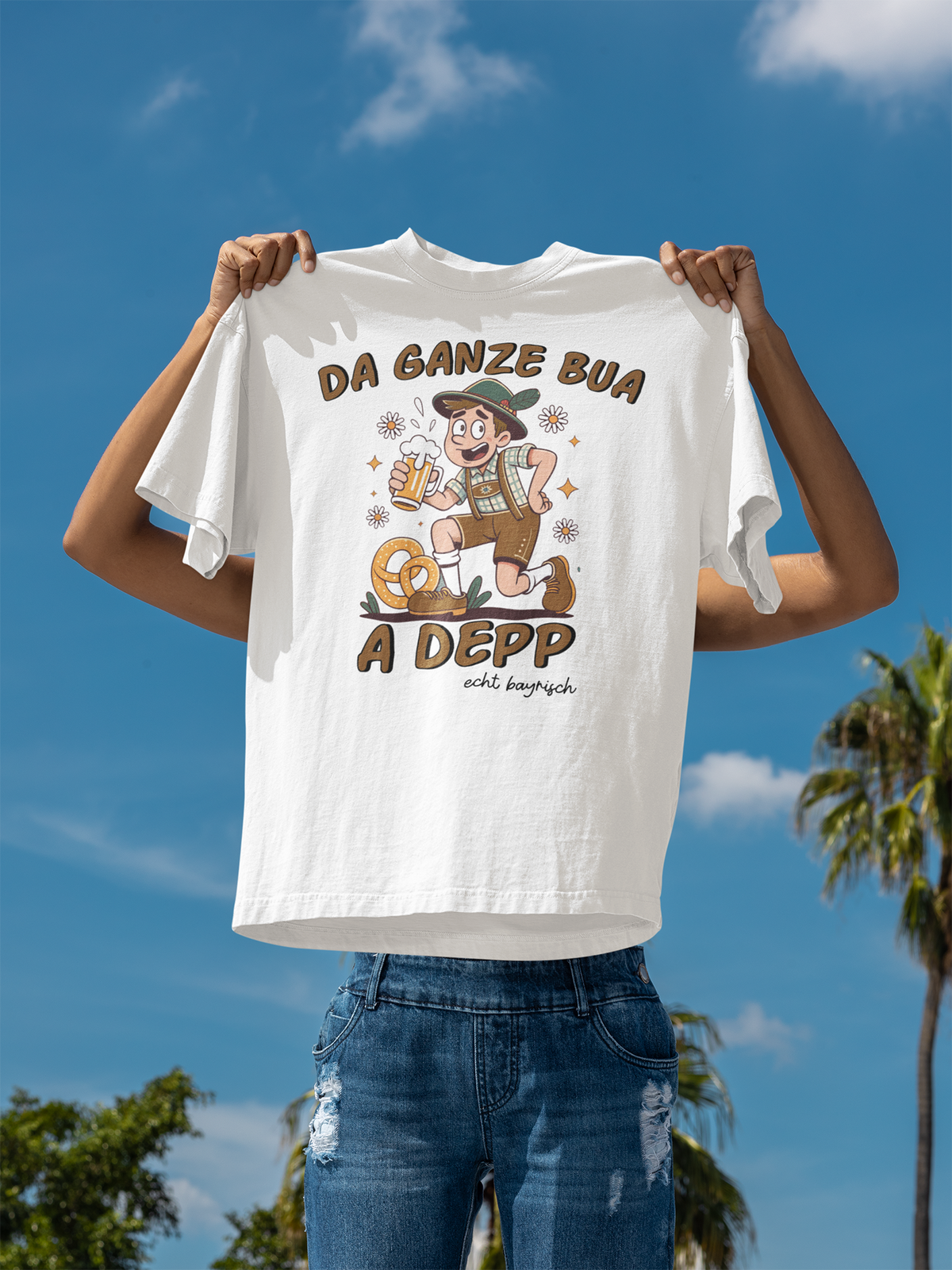 Weißes T-Shirt mit Motiv: bayerischer Mann mit Maßkrug und Spruch „Da ganze Bua a Depp“, es wird von zwei Armen in die Höhe gehalten