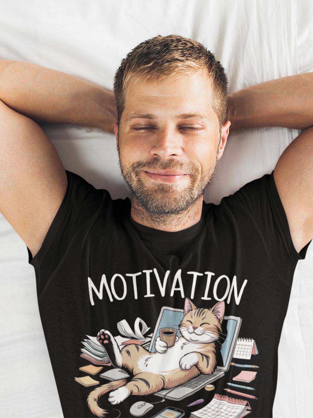 Mann, liegend mit geschlossenen Augen, trägt schwarzes T-Shirt mit Comic-Motiv: Katze schläft auf Laptop im Zettelchaos, Oberkörperansicht