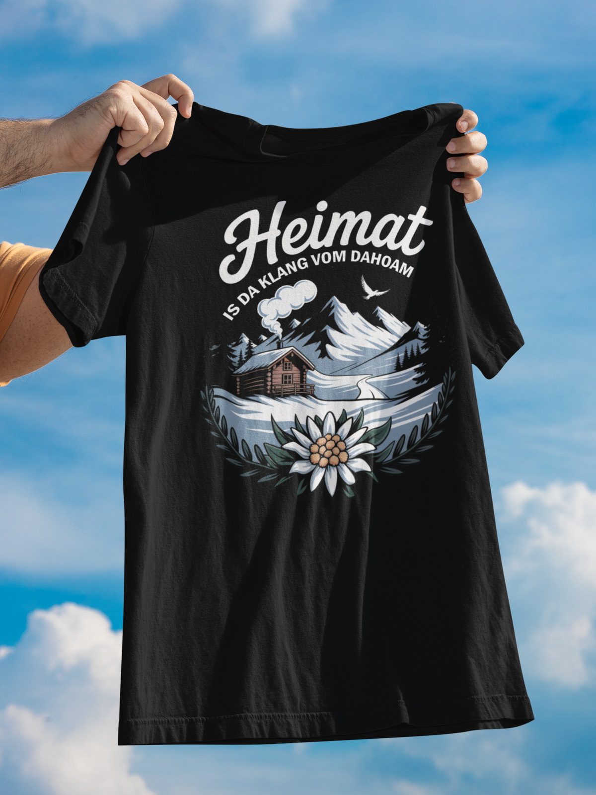 Schwarzes Shirt wird in die Luft gehalten. Aufdruck: Heimat, mit Bergmotiv