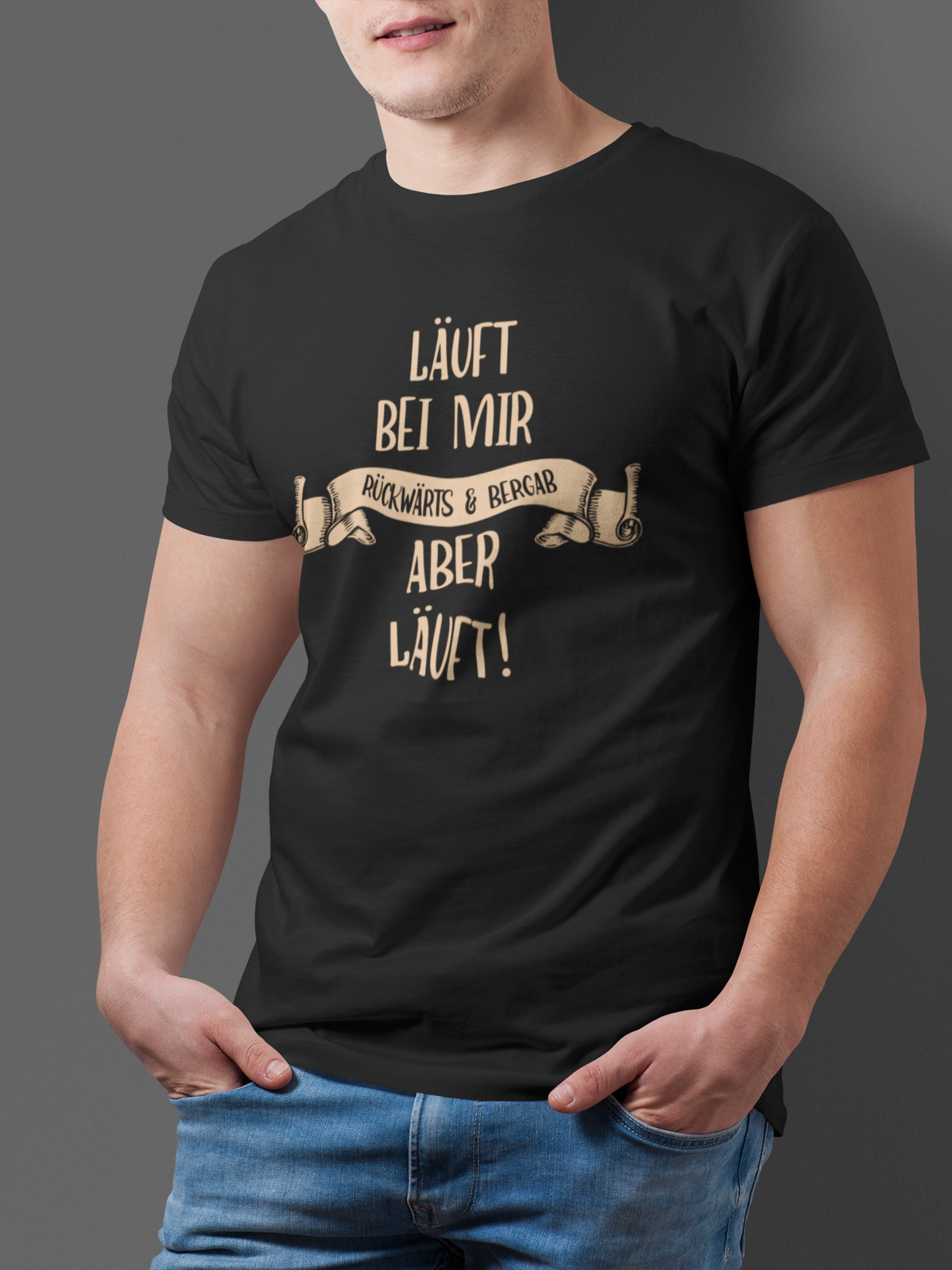 Junger Mann trägt schwarzes T-Shirt mit dem weißen Text „Läuft bei mir. Rückwärts und bergab. Aber läuft!“