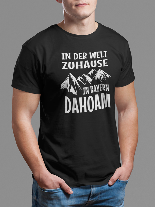 Junger Mann trägt schwarzes T-Shirt mit weißen Text: In der Welt zuhause. in Bayern dahoam. Oberkörperansicht