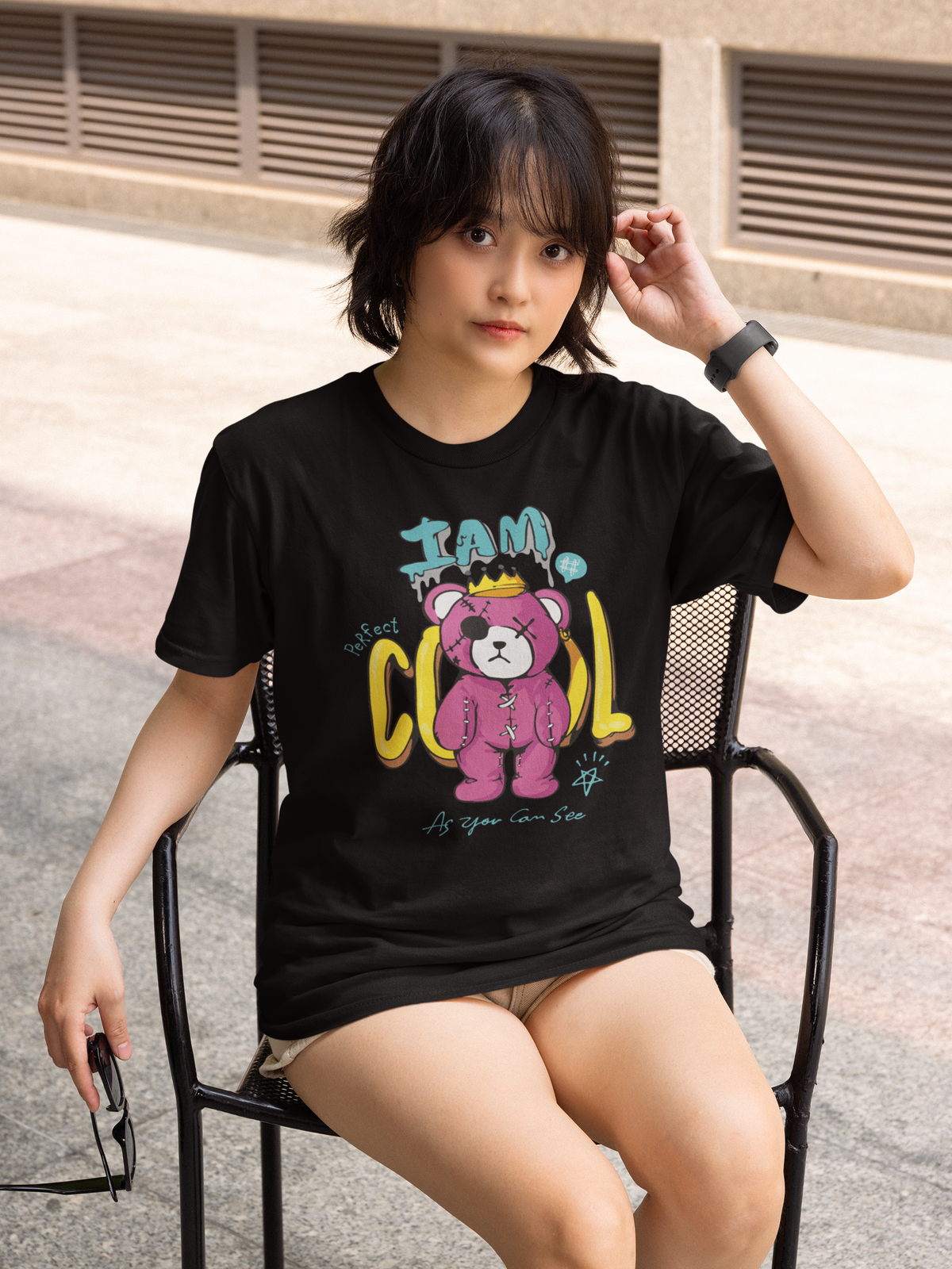 Junge Frau, sitzend auf Stuhl, trägt schwarzes T-Shirt mit Teddy-Motiv (Oberkörperaufnahme)