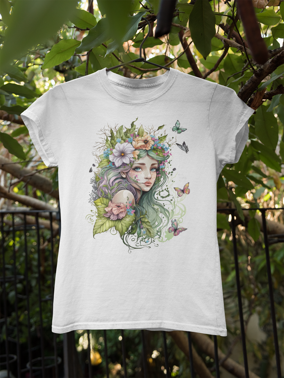 Weißes T-Shirt mit gezeichneter Waldelfe, umgeben von grünen Pflanzen, Blumen und Schmetterlingen. Im Hintergrund grüne Blätter.
