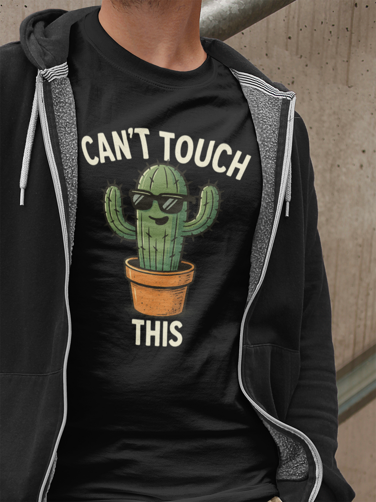 Oberkörper eines Mannes mit schwarzer offener Jacke. Darunter ein schwarzes T-Shirt mit Cartoon-Kaktus und Spruch „Can’t Touch This“.