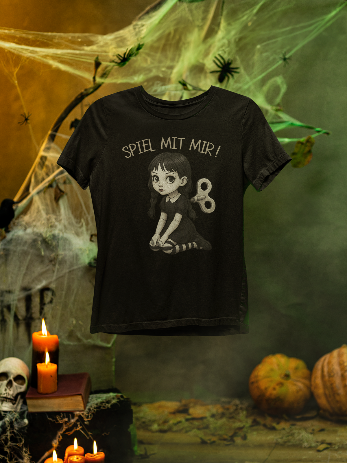 Schwarzes T-Shirt mit Aufschrift "Spiel mit mir!" und Gothic Doll Motiv. Im Hintergrund Spinnenweben und Halloween-Dekoration, Kerzen und Kürbisse.