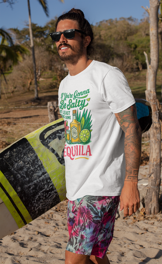 Mann steht am Strand mit Surfbrett unterm Arm und trägt ein weißes T-Shirt mit tropischem Tequila-Motiv