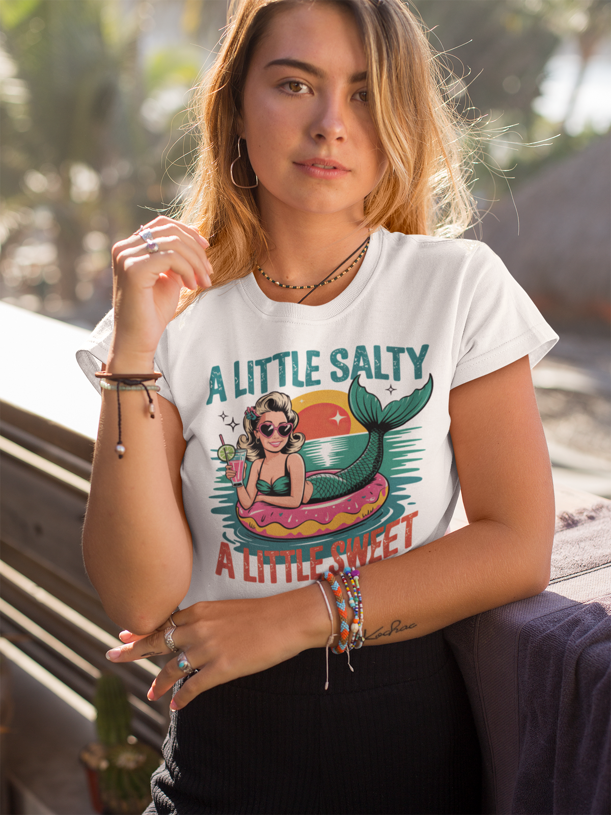 Blonde junge Frau mit weißem Shirt mit Aufschrift "A little salty" und Meerjungfra-Motiv.