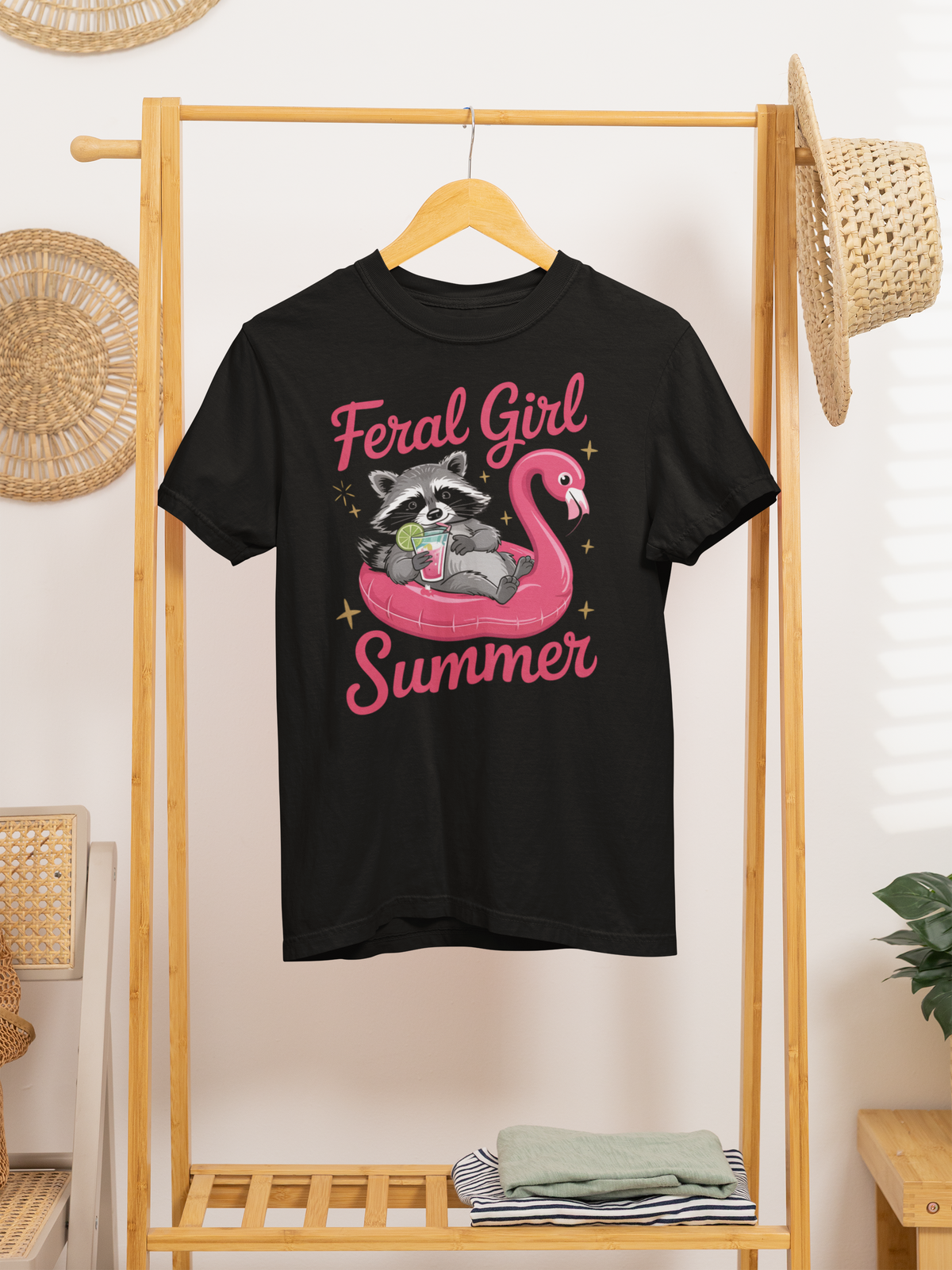 T-Shirt mit Waschbär auf pinkem Flamingo-Schwimmreifen, Cocktail in der Pfote und Schriftzug „Feral Girl Summer“