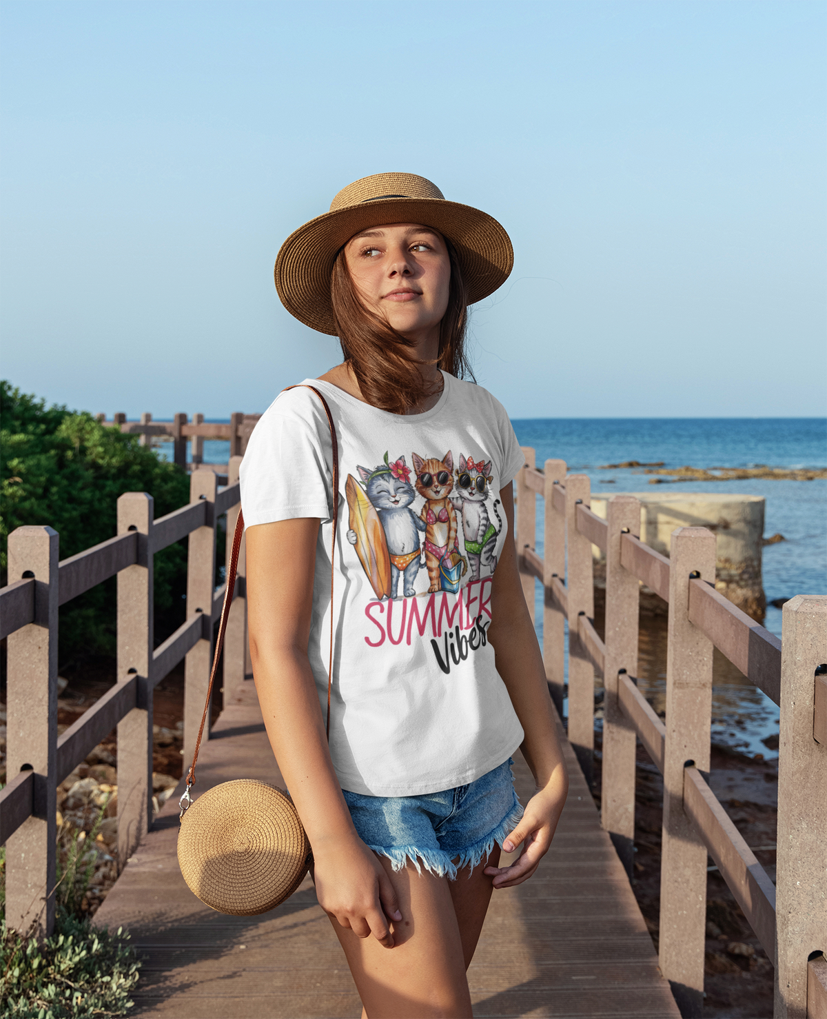 Frau auf Steg am Meer mit Sonnenhut. Sie trägt ein Shirt mit Katzen-Motiv.