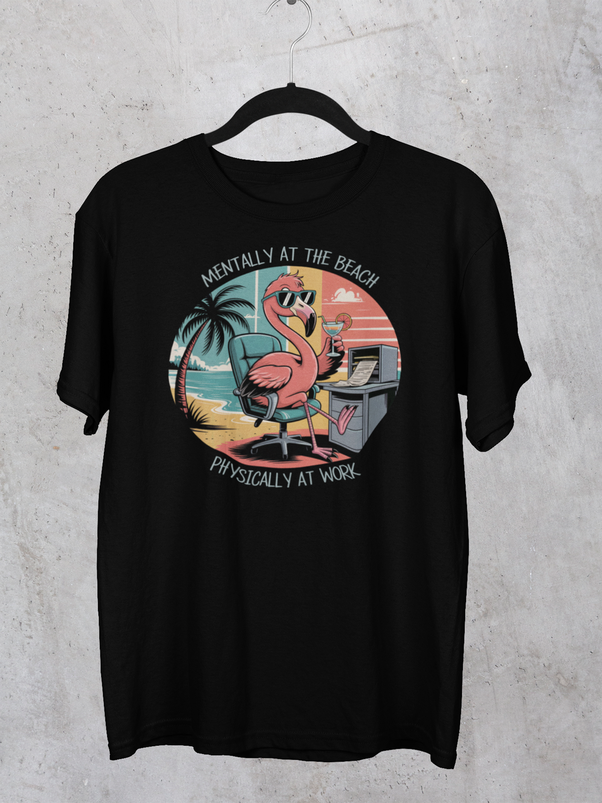 Schwarzes Shirt mit Flamingo-Motiv hängt auf schwarzen Kleiderbügel vor grauer Wand.