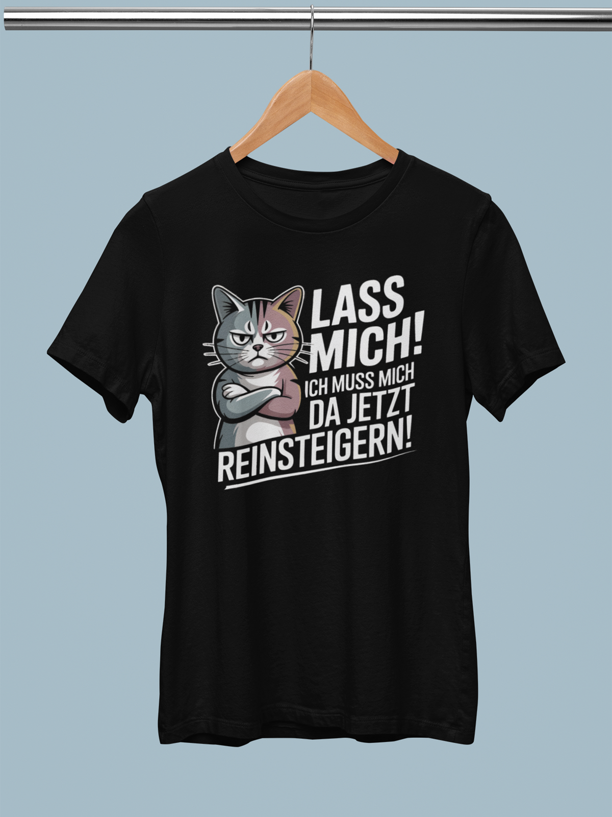 Auf einer Stange hängt ein schwarzes T-Shirt mit Katzenmotiv und der Aufschrift "Lass mich! Ich muss mich da jetzt reinsteigern!"