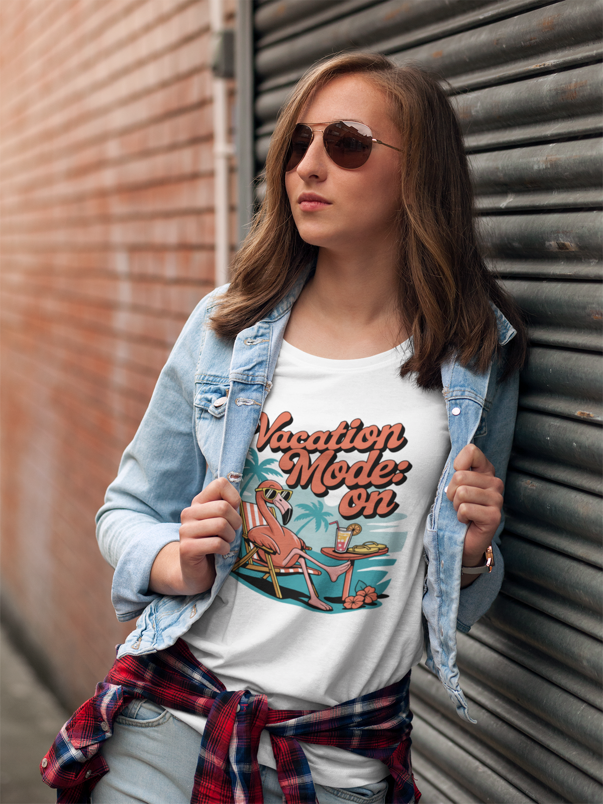 Junge Frau mit Sonnebrille und offener Jeansjacke trägt ein weißes T-Shirt mit dem Motiv „Vacation Mode: On“ und einem Flamingo mit Sonnenbrille, Oberkörperansicht