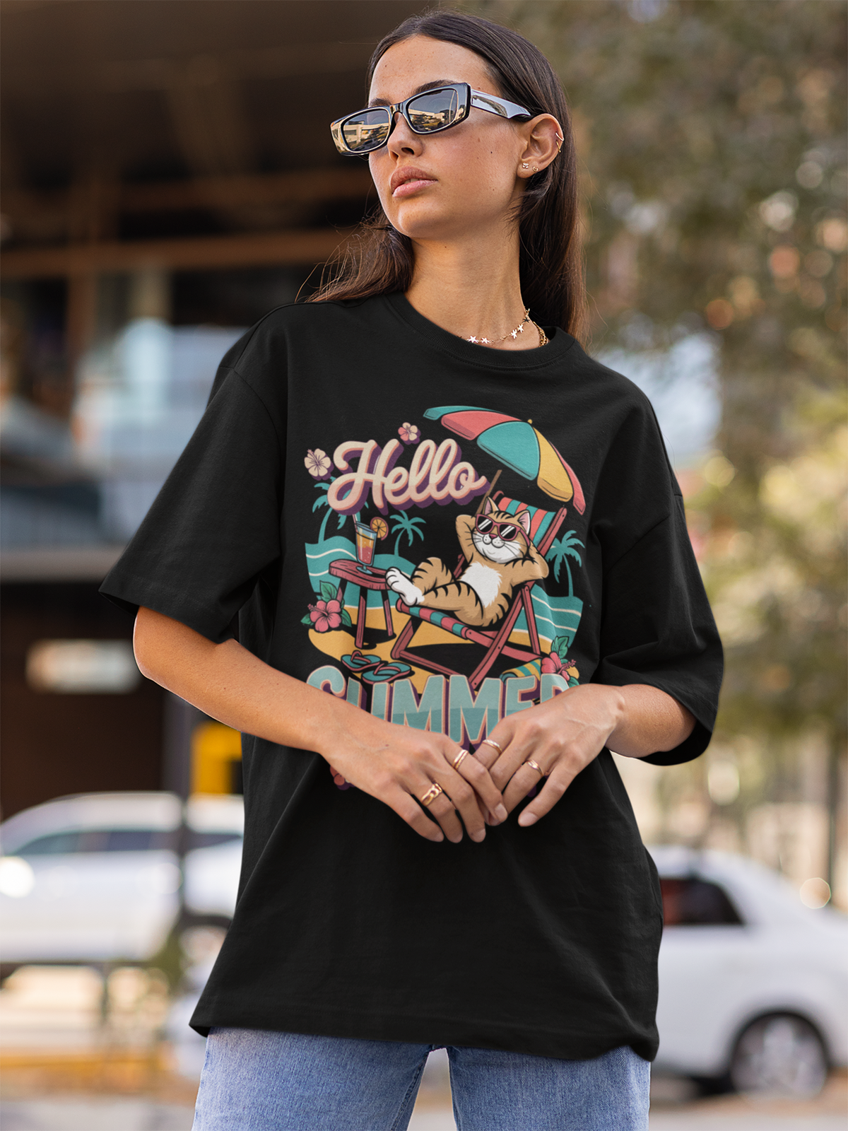 Junge Frau mit Sonnenbrille und langen schwarze Haaren trägt ein Oversize T-Shirt in schwarz mit Sommer Katzen-Motiv