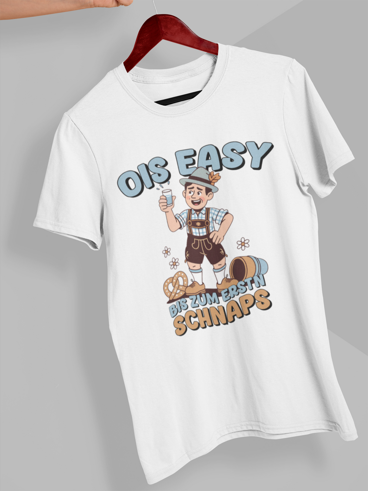 Weißes T-Shirt auf Kleiderbügel hängend mit Comic-Motiv und bayerischem Spruch „Ois easy bis zum erstn Schnaps“