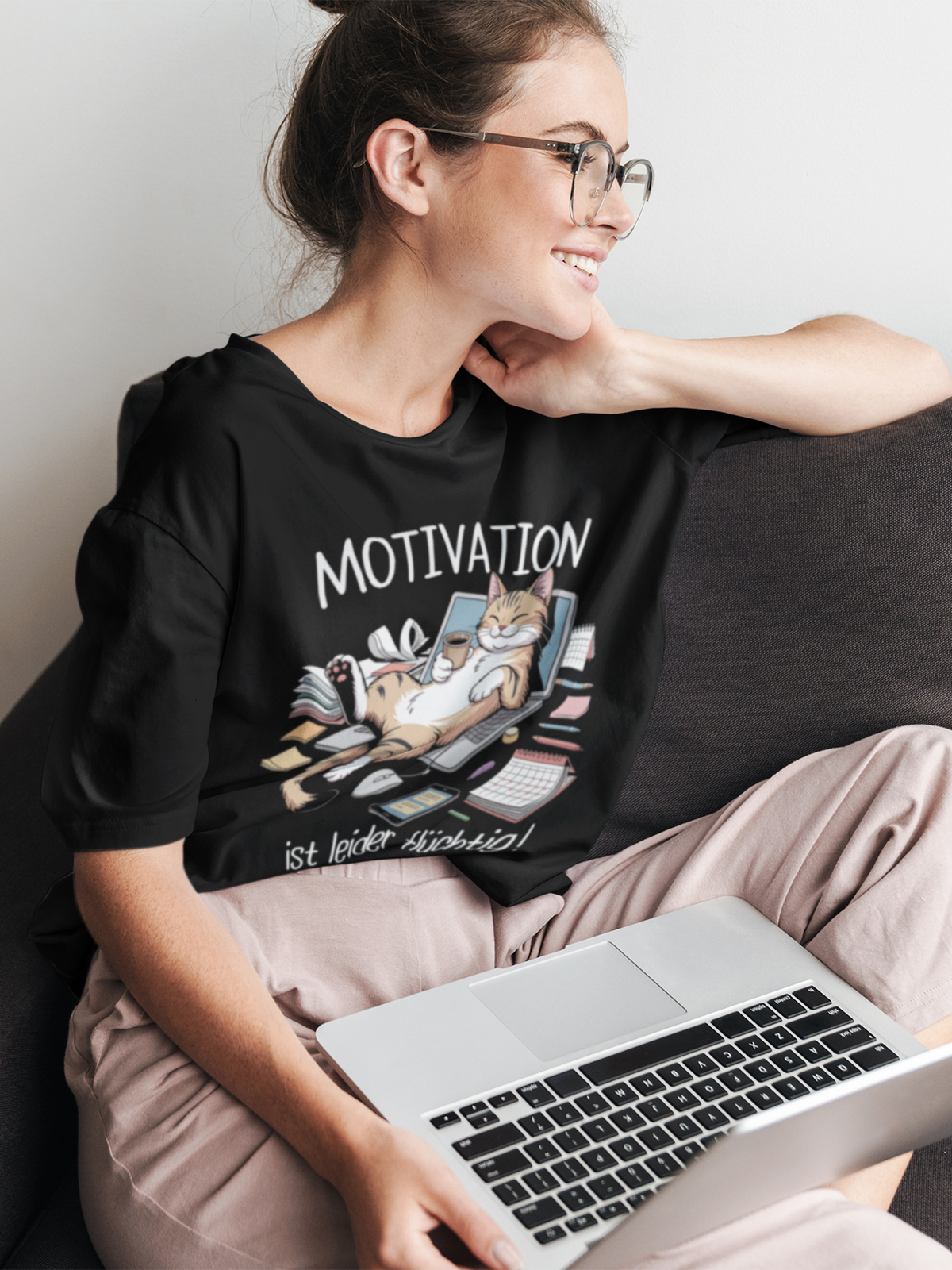 Frau mit Laptop auf dem Schoß, trägt schwarzes T-Shirt mit Comic-Motiv: Katze schläft auf Laptop im Zettelchaos, Oberkörperansicht