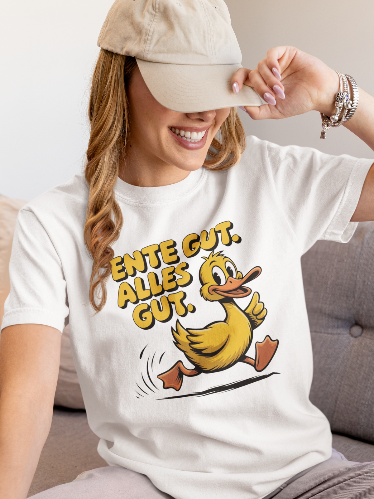 Junge lachende Frau mit Schirmmütze trägt weißes T-Shirt mit Ente und dem Spruch „Ente gut, alles gut“ (Oberkörperaufnahme)