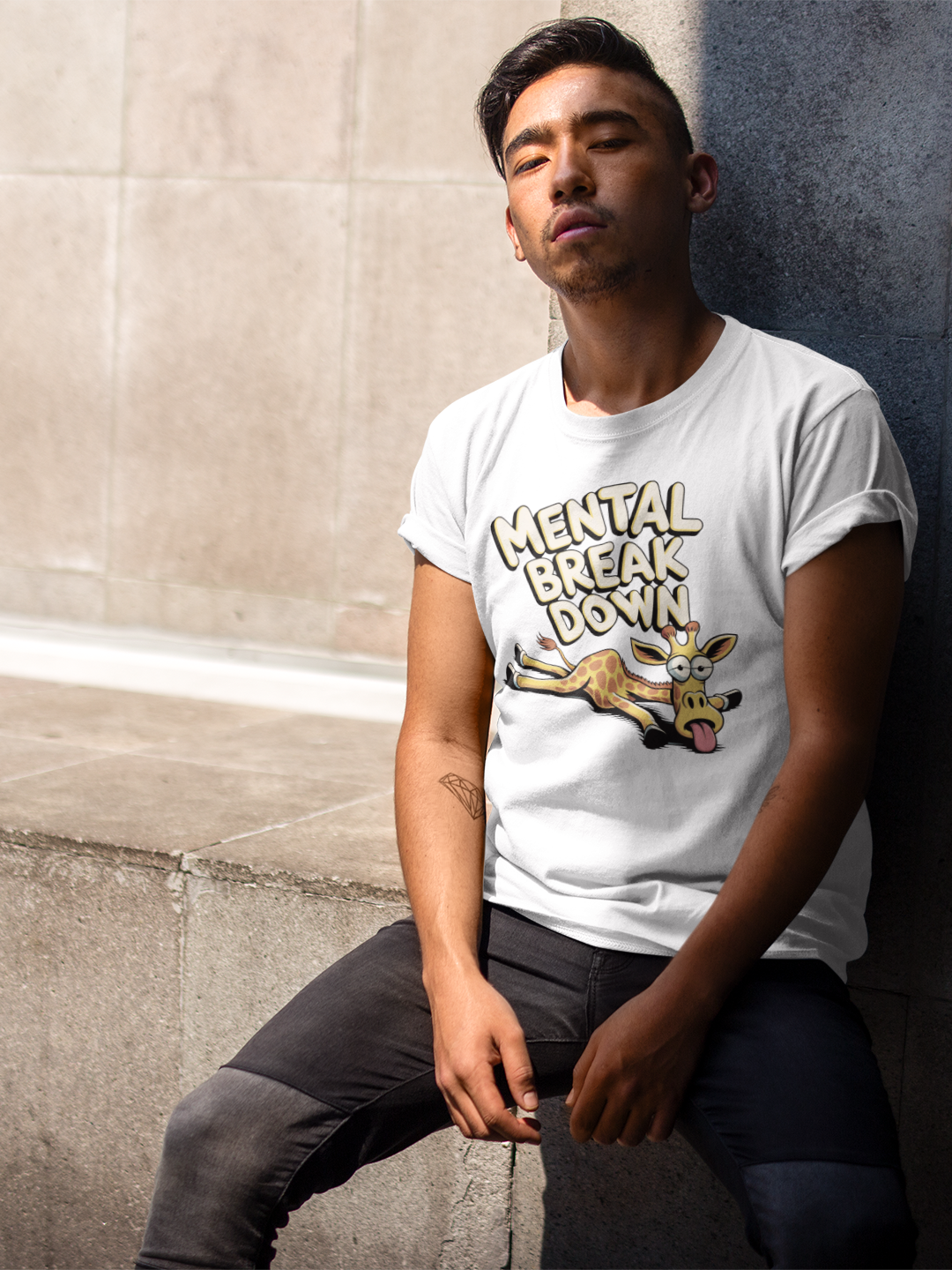Junger Mann, an Mauer sitzend, trägt weißes T-Shirt mit Giraffe und dem Text „Mental Break Down“ (Oberkörperaufnahme)