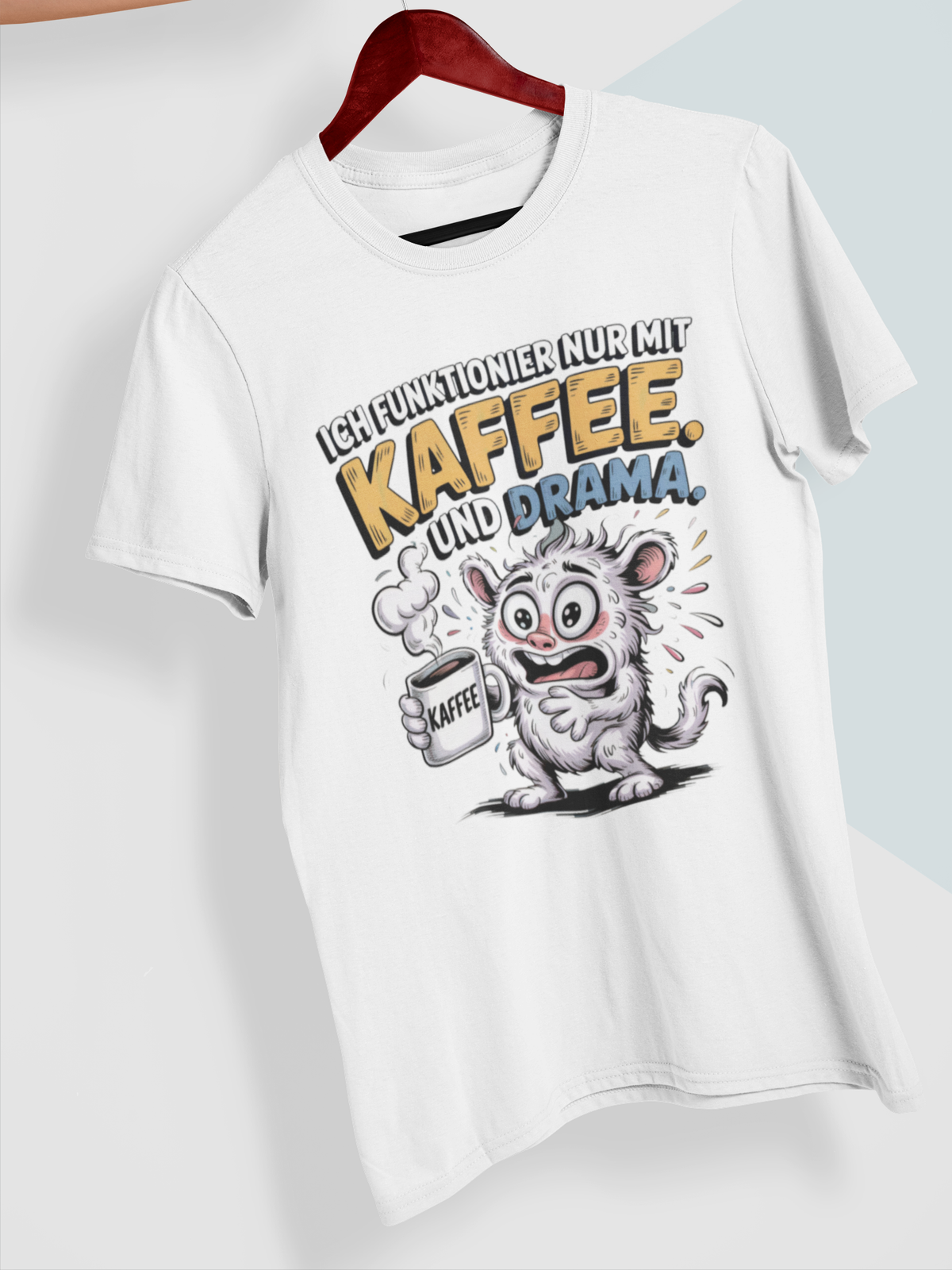Weißes T-Shirt mit verrücktem Monster und dem Text „Ich funktionier nur mit Kaffee und Drama“ auf Kleiderbügel