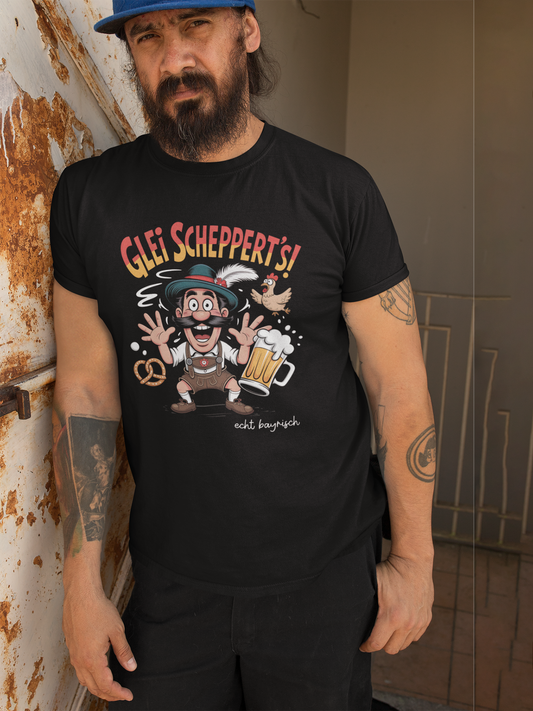 Mann mit Bart und Tattoos trägt ein schwarzes T-Shirt mit Aufschrift "Glei schppert´s. Echt bayrisch" und Bayern-Motiv: Mann in Lederhose und Masskrug.