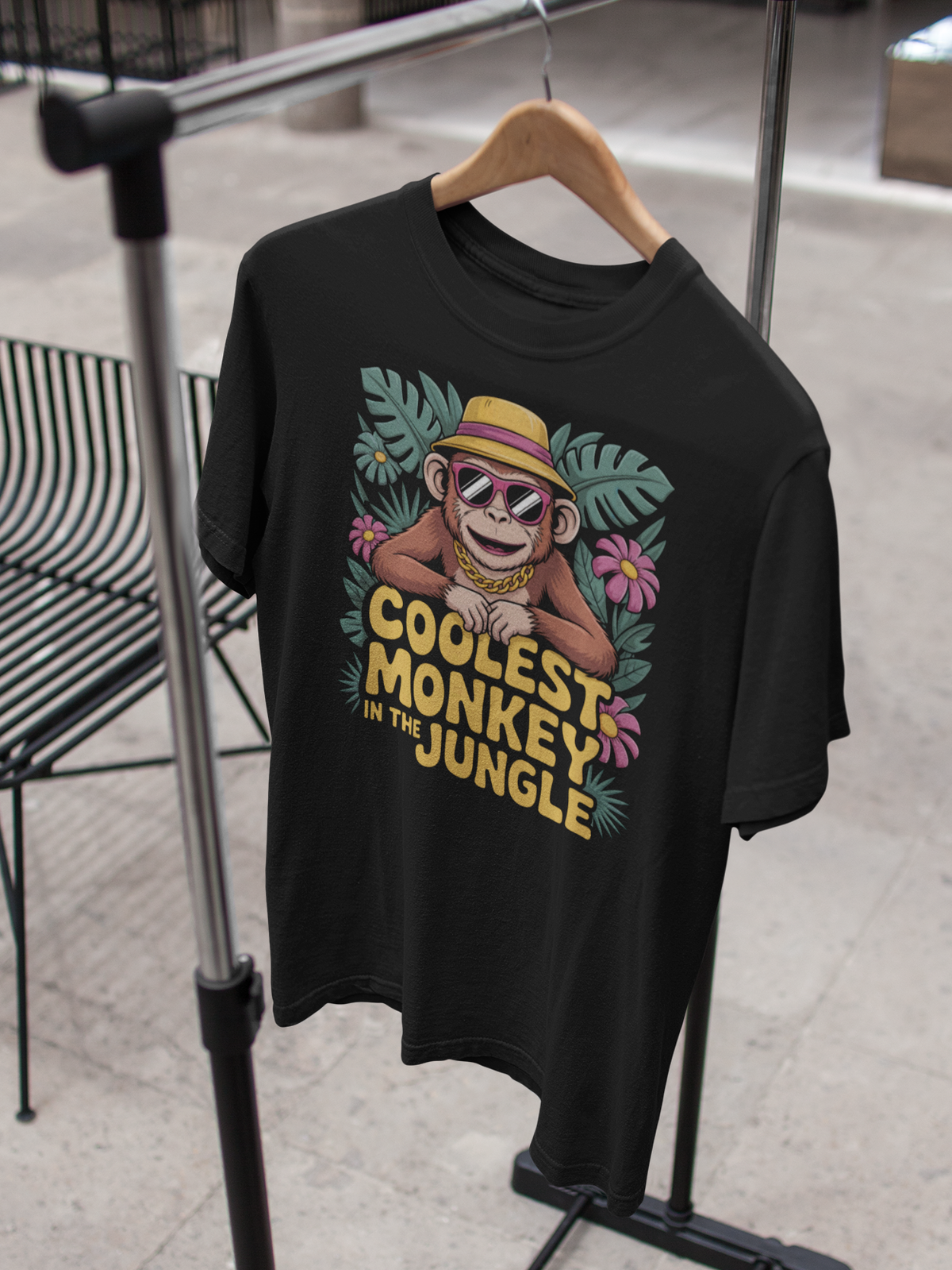 Schwarzes T-Shirt mit Affe mit Sonnenbrille und Hut, und Text „Coolest Monkey in the Jungle“, T-Shirt hängt auf Kleiderständer