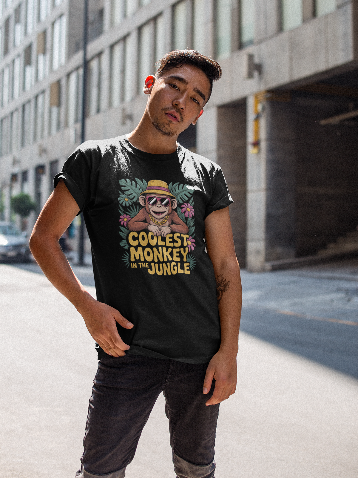 Junger Mann auf der Straße. Er trägt ein schwarzes T-Shirt mit Affe mit Sonnenbrille und Hut, und Text „Coolest Monkey in the Jungle“