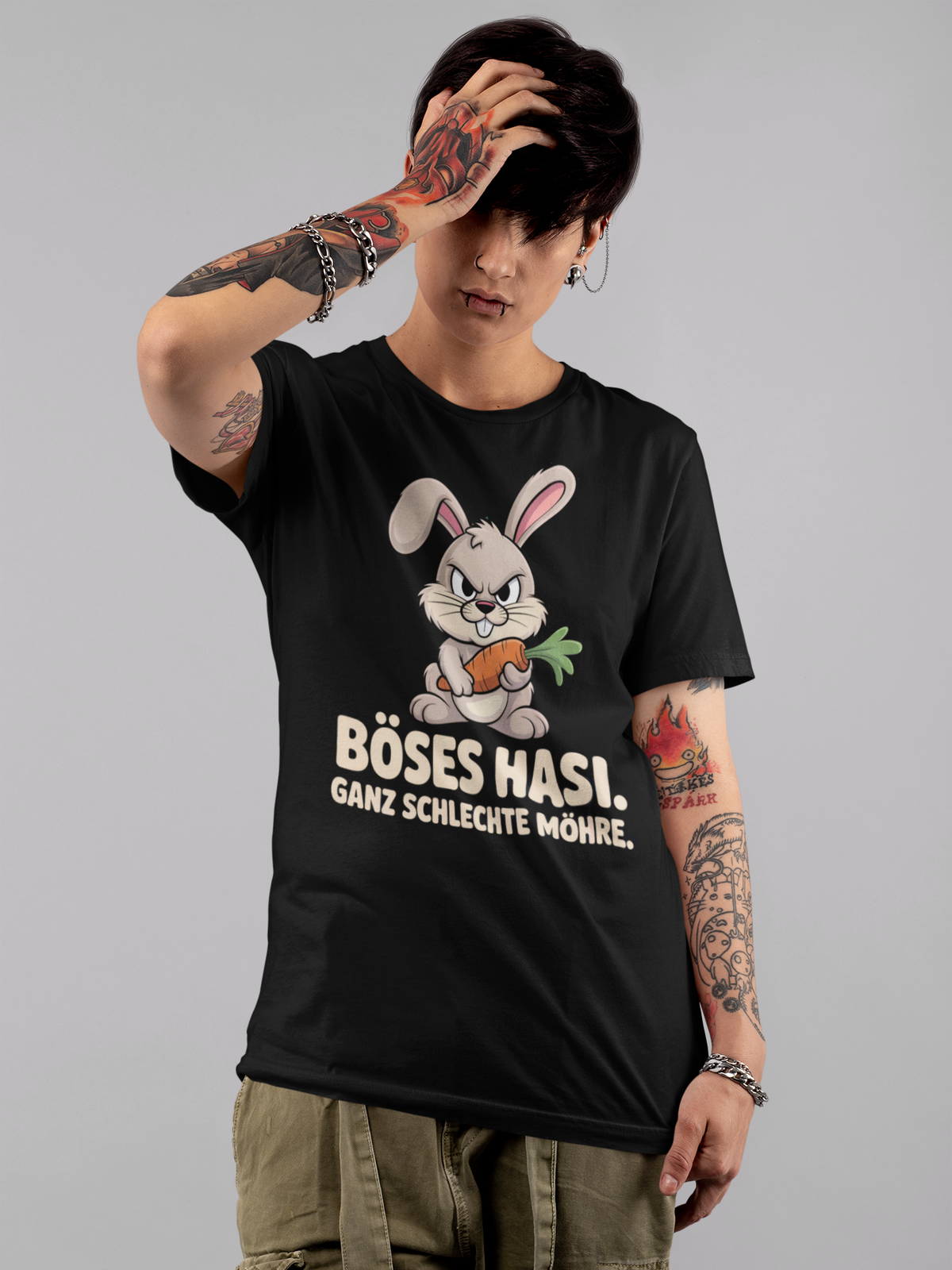 Junge Frau, kurze schwarze Haare, tättowiert, trägt schwarzes Shirt mit frechem Hasen und Spruch (Oberkörperaufnahme)