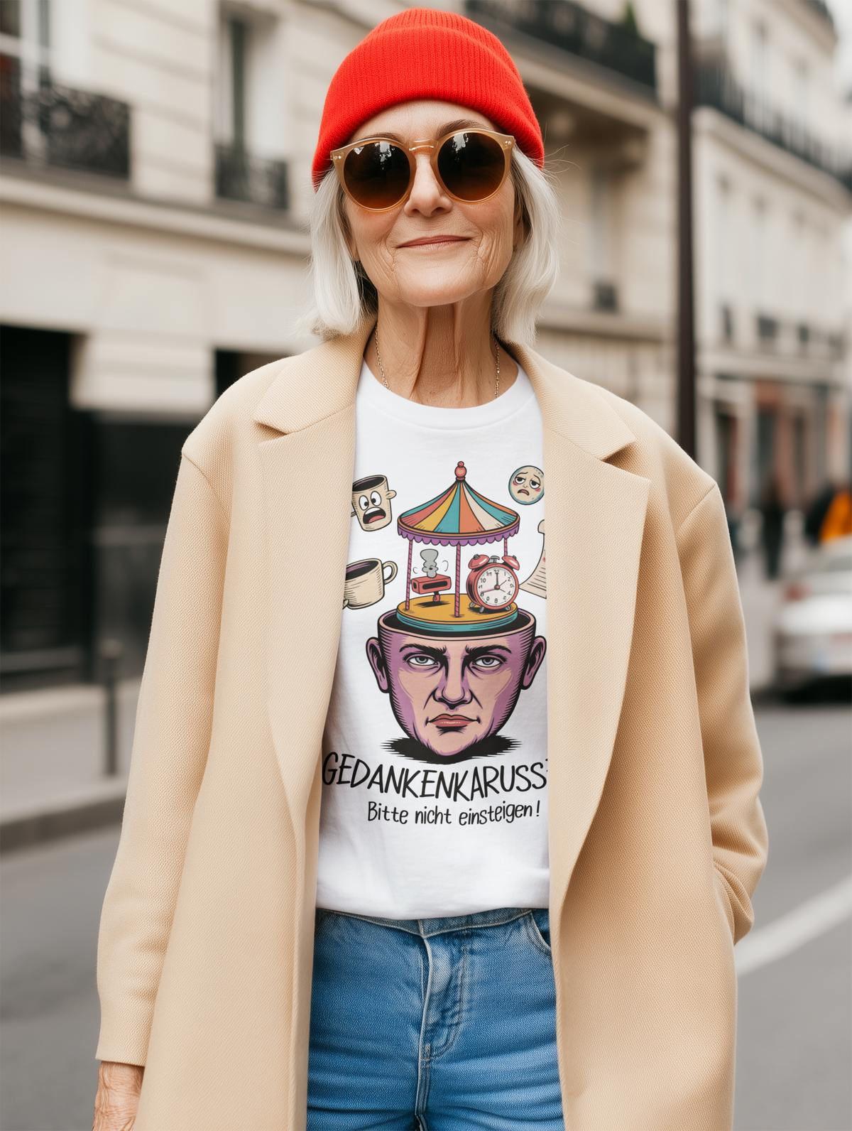 Frau mit oranger Mütze und offenen beigen Mantel. Darunter trägt sie ein weißes T-Shirt mit Text „Gedankenkarussell – Bitte nicht einsteigen“ und Karssell-Kopf-Motiv.