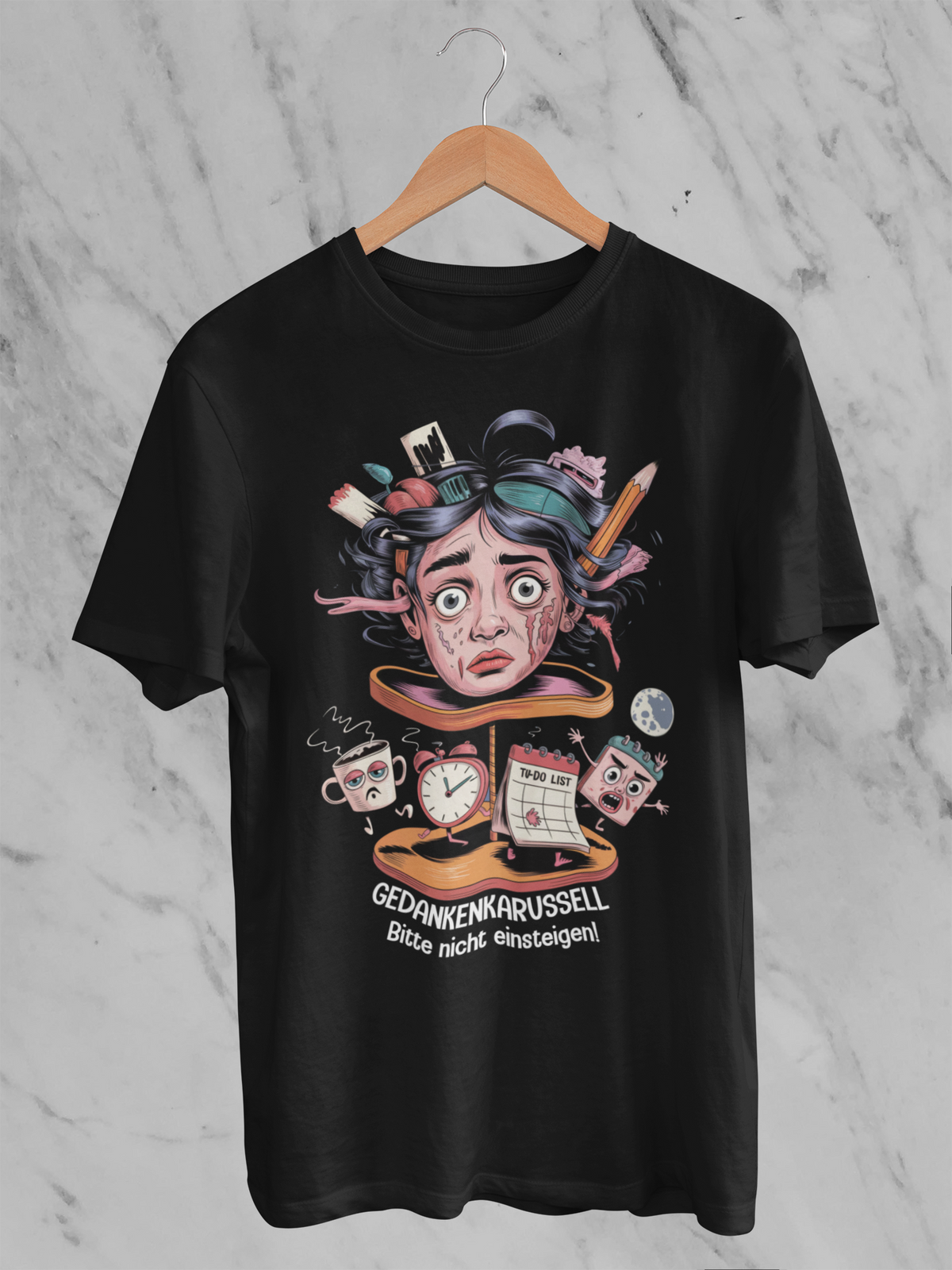 Schwarzes T-Shirt auf Kleiderbügel  mit surrealistischem Kopf-Karussell-Motiv und weißem Text „Gedankenkarussell – Bitte nicht einsteigen“
