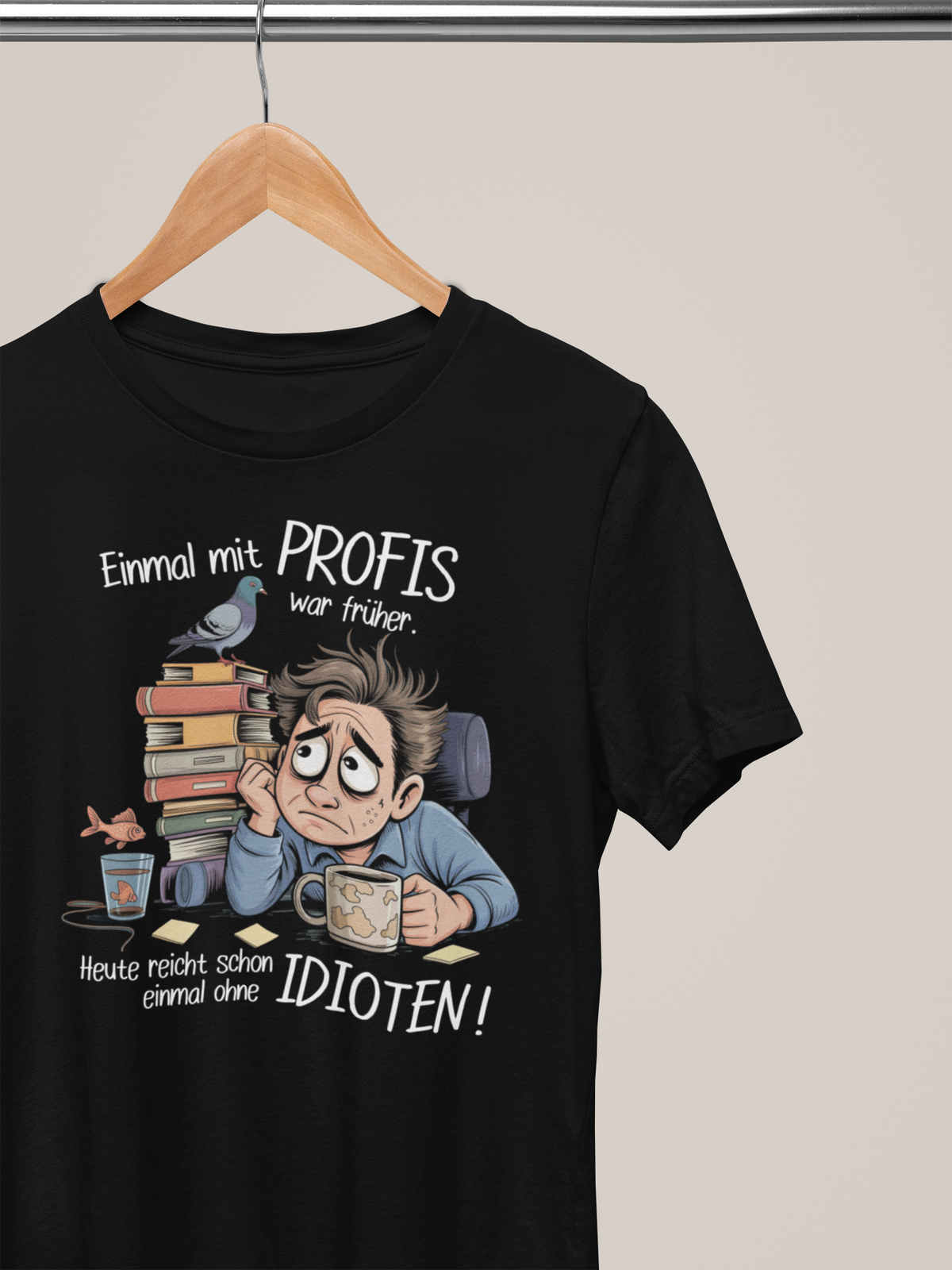 Schwarzes T-Shirt auf Kleiderbügel mit weißem Spruch „Einmal mit Profis war früher – Heute reicht schon ohne Idioten“ und Comic-Büro-Motiv.