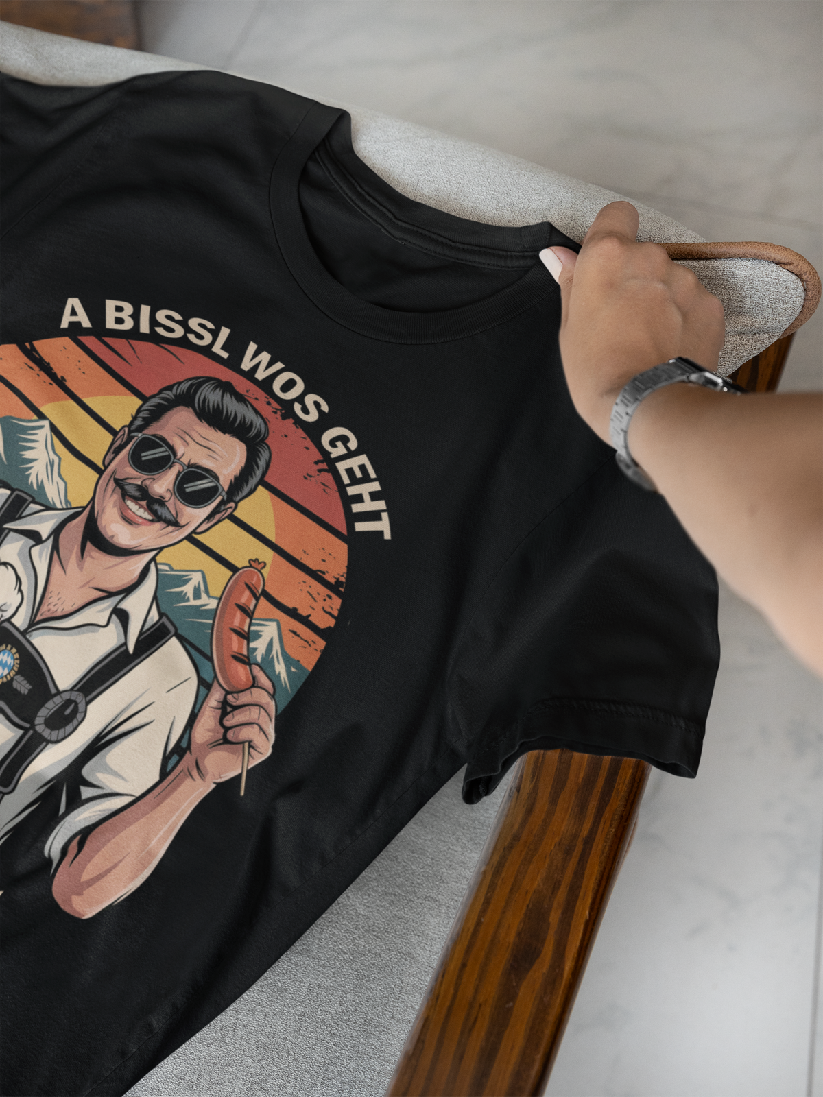 Schwarzes T-Shirt, liegend, mit Spruch „A bissl wos geht oiwei nu“ und Retro-Motiv mit bayerischem Mann, Maß und Bratwurst