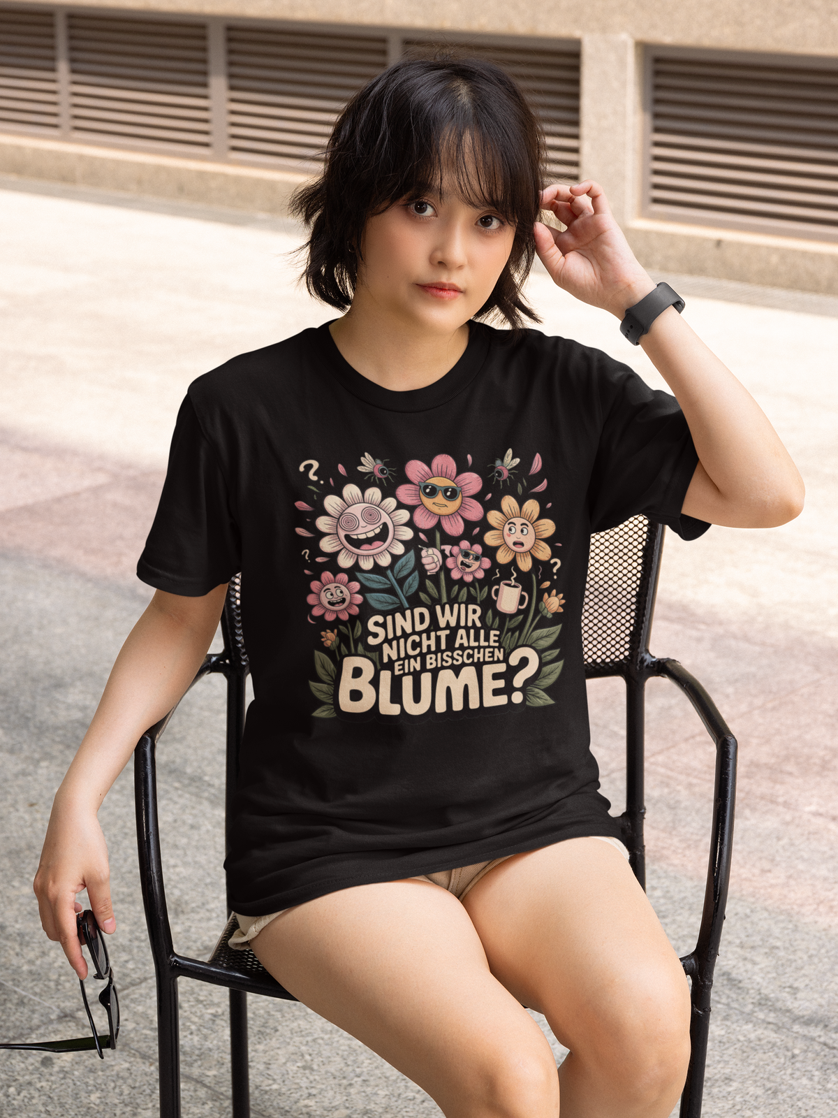 Ganzkörperaufnahme einer Frau, auf Stuhl sitzend, mit Shirt mit dem Spruch „Sind wir nicht alle ein bisschen Blume?“