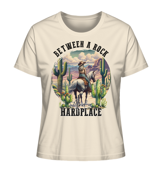 Beiges Damen-T-Shirt mit Motiv: Cowgirl auf Pferd in Wüstenlandschaft mit Kakteen und Schriftzug „Between a rock and a heardplace“