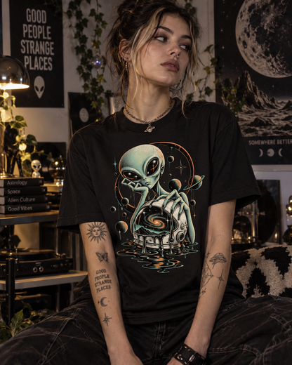 Weibliches Model trägt schwarzes T-Shirt mit Gelangweilter Alien mit geöffnetem Helm, kosmischem Wirbel und Planeten