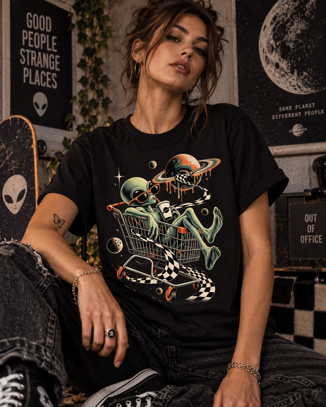 Weibliches Model trägt schwarzes T-Shirt mit Alien im Einkaufswagen mit Planeten und Schachbrettband