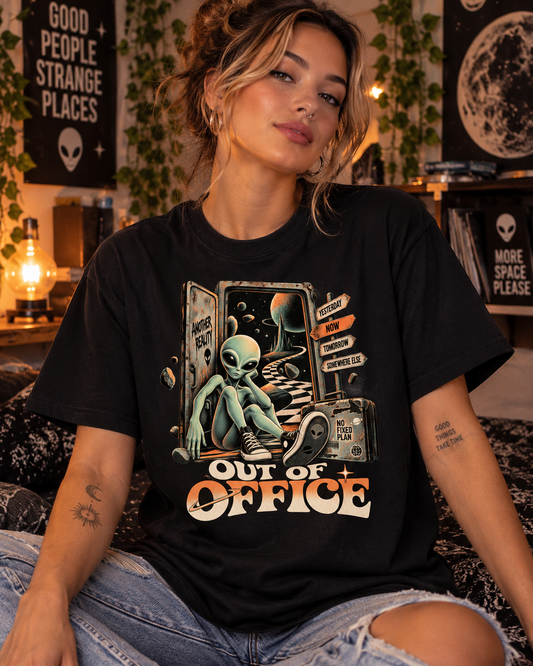 Weibliches Model trägt schwarzes T-Shirt mit Entspannter Alien vor einem offenen Weltraumportal mit Out of Office