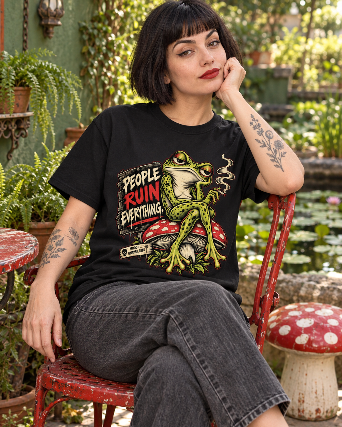 Frau trägt das People Ruin Everything Frosch T-Shirt auf einem roten Stuhl im Garten