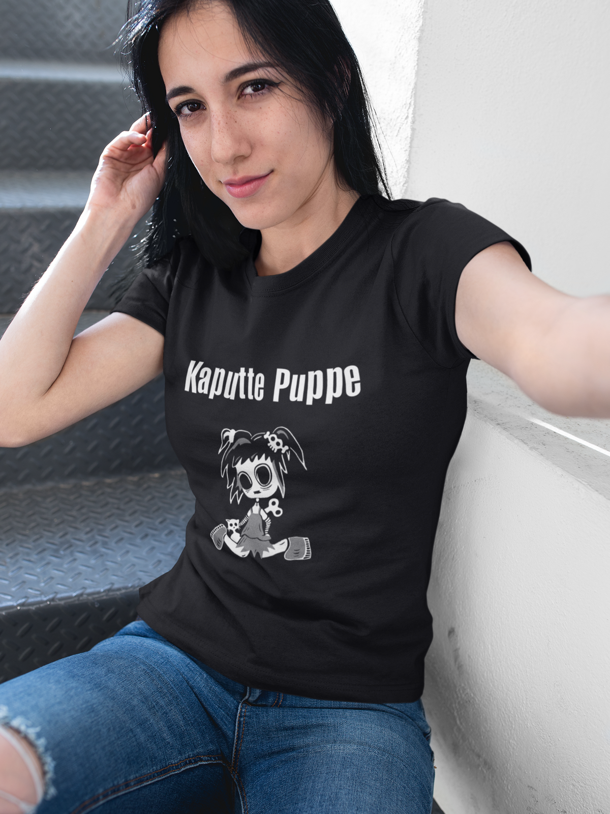 Gothic-Frau mit schwarzen Haaren trägt das T-Shirt „Kaputte Puppe“ mit Gothic-Doll-Motiv und schaut direkt in die Kamera