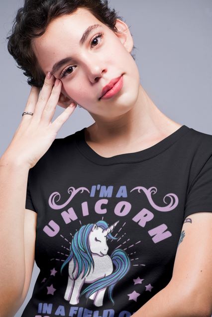 Frau, nachdenklich, trägt Schwarzes T-Shirt mit pastellfarbenem Einhorn und Spruch „I’m a unicorn in a field of horses“ – magisch, bezaubernd, einzigartig.